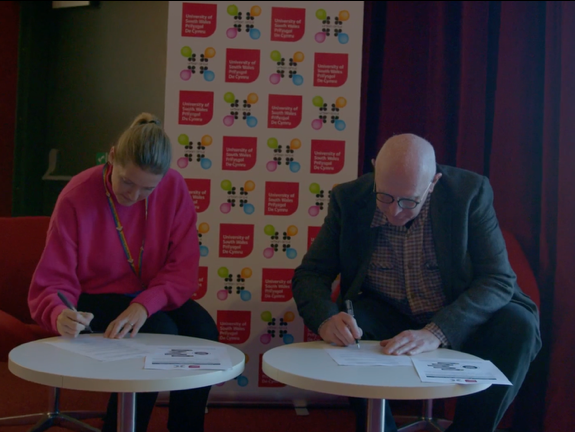 two people from the university of south wales signing a piece of paper honoring our partnership
